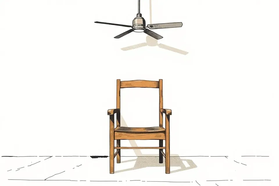 An empty wooden chair on a concrete floor, with a motionless ceiling fan above, casting a long shadow.